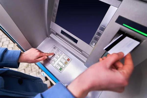 Közeli kép egy bankautomatáról, miközben valaki kártyát használ és gombot nyom meg.