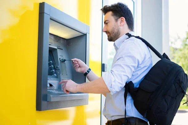 Férfi egy bankautomatát használ, hátizsákkal a vállán.
